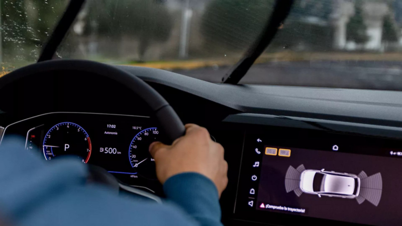 Conductor sujeta volante de Volkswagen bajo lluvia y ve cuadro de instrumentos.