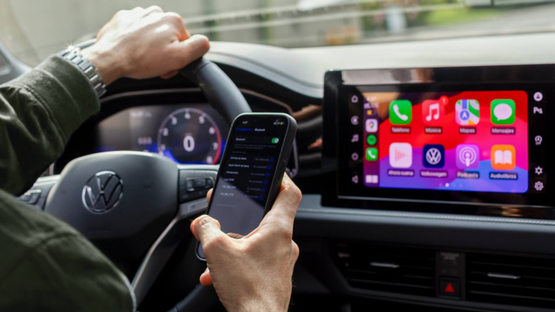 Conductor sostiene un celular frente a la pantalla con Apple CarPlay.