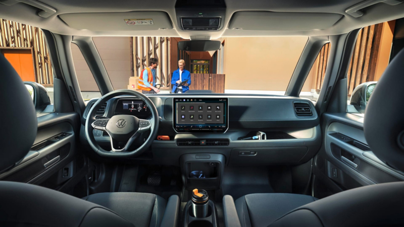 Vista del salpicadero de una furgo VW vista desde el asiento de atrás y unas personas de pie en frente.