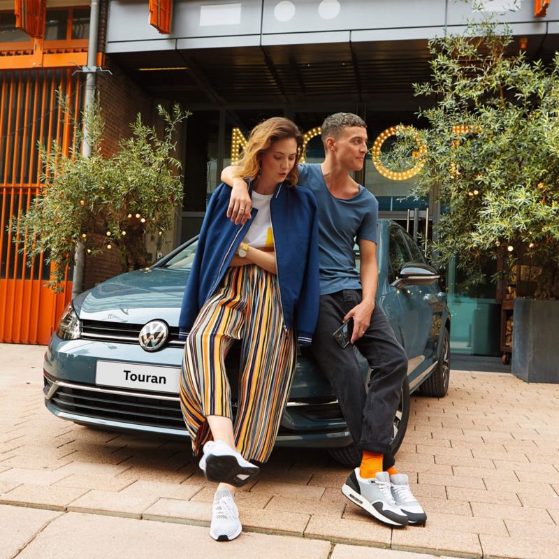 A couple leaning on the front of a VW Golf bonet