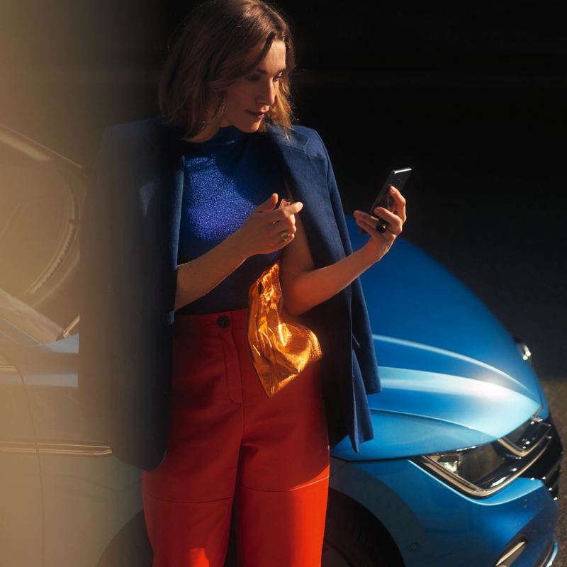 A woman holding a mobile phone leaning on a VW vehicle