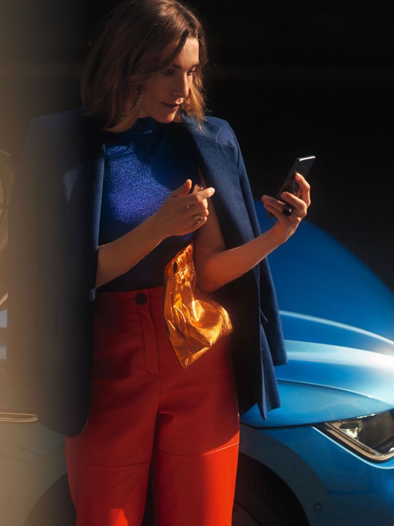 A woman holding a mobile phone leaning on a VW vehicle