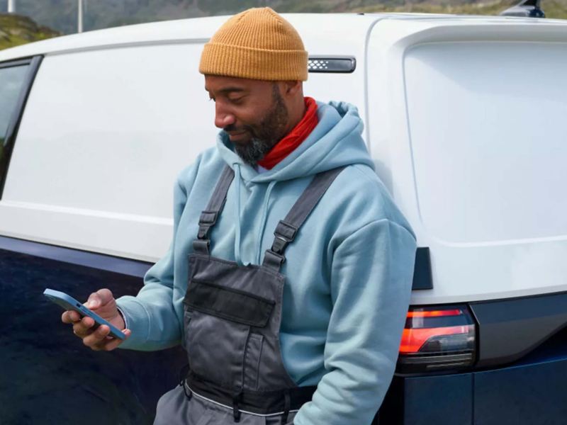 a man leaning against a VW EV vehicle checking his phone