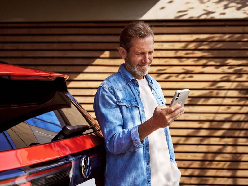 A man leaning on a Volkswagen Tiguan and looking at his phone