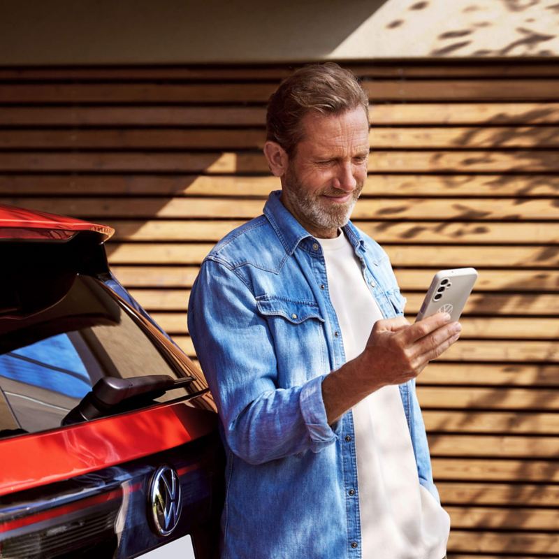 A man leaning on a Volkswagen Tiguan and looking at his phone