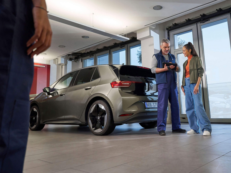 Un technicien Volkswagen et une cliente discutent derrière une ID.3.