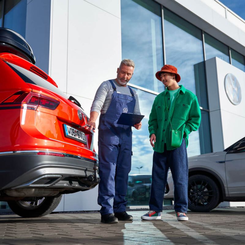 Une technicien Volkswagen et un client discutent derrière un Tiguan rouge.