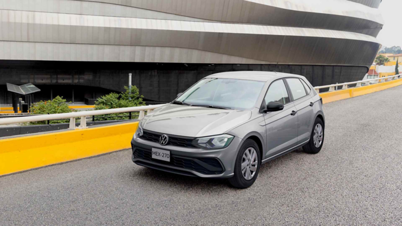 Carro Volkswagen de color gris circula en una avenida elevada cercana a plaza comercial. 