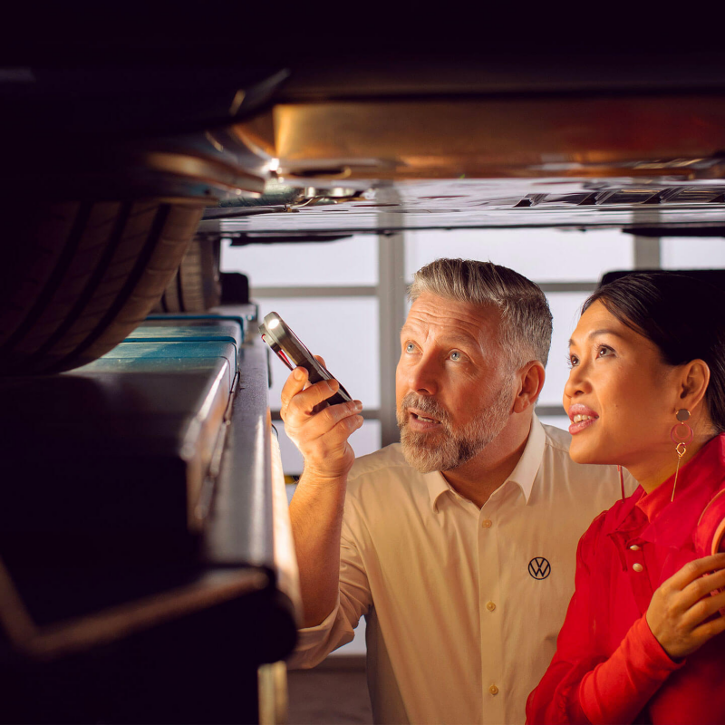 Un technicien Volkswagen et une femme observe le soubassement d'une voiture lors du contrôle technique.