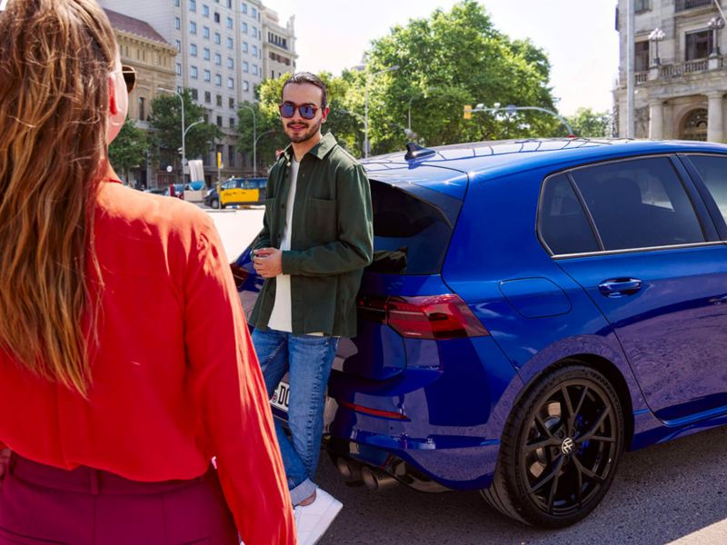 Une femme rejoint un homme, près de sa Volkswagen Golf.