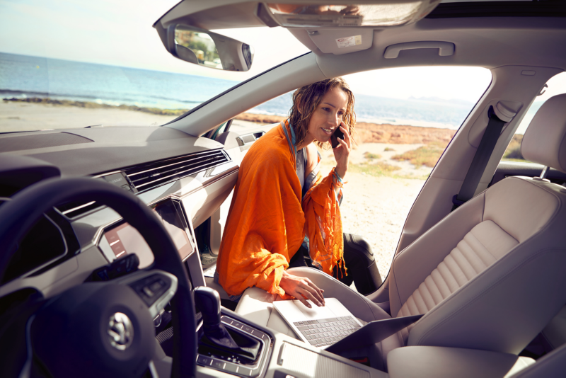 Woman inside car looking at laptop and on the phone