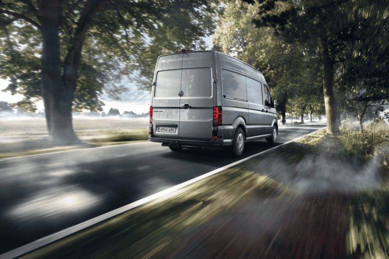 VW Crafter jedzie drogą wśród drzew.