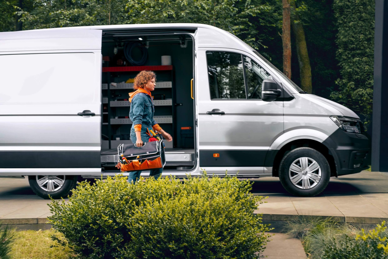 Une femme qui porte une trousse à outils marche à côté d'un VW Sprinter blanc