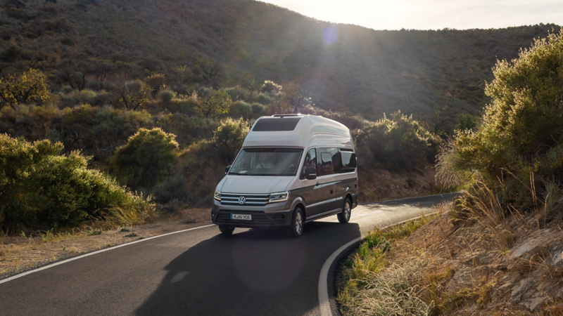 Un VW Grand California roule sur une route sinueuse.