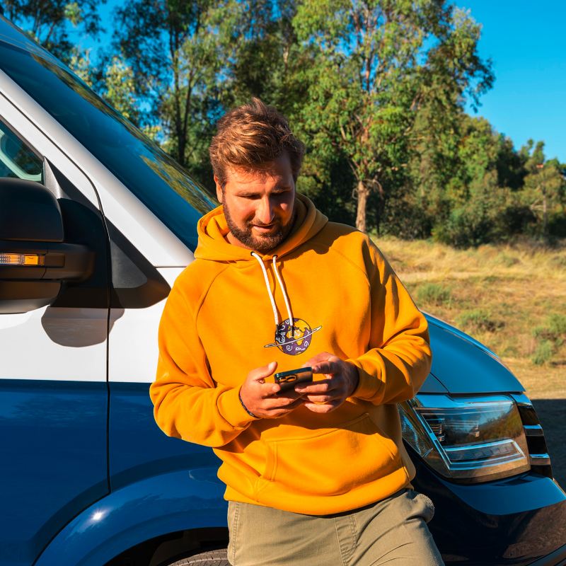 Man står vid en VW Grand California med en smartphone i handen