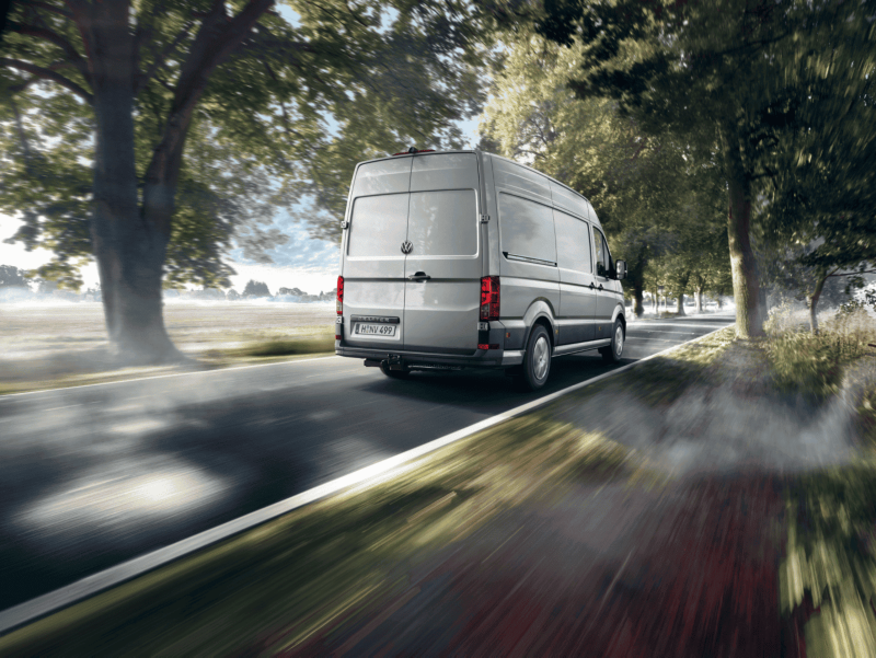 Volkswagen Crafter Furgon jedzie po drodze asfaltowej między drzewami.