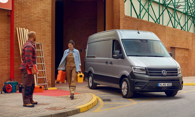 zwei Handwerker die Werkzeug aus einem VW Crafter Kastenwagen holen der vor einer Lagerhalle steht.