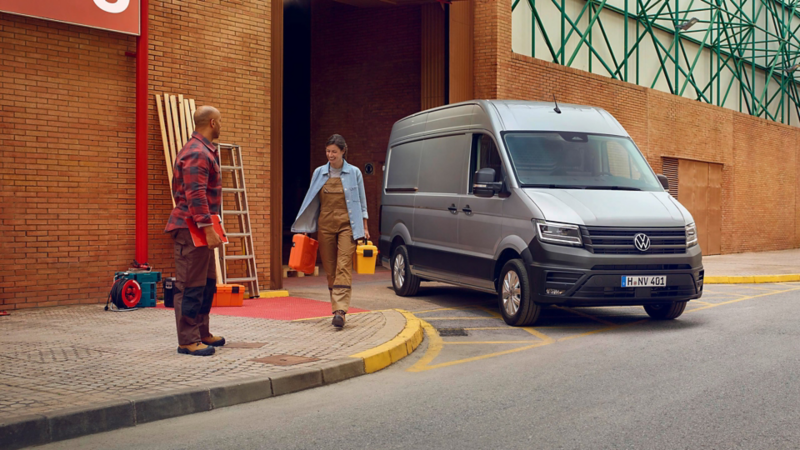 Bauarbeiter:innen vor einem Firmengebäude, VW Crafter verlässt Gebäude.