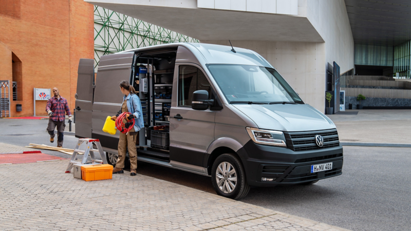 Eine Handwerkerin räumt Werkzeuge aus einem VW Crafter aus, welcher am Straßenrand parkt.
