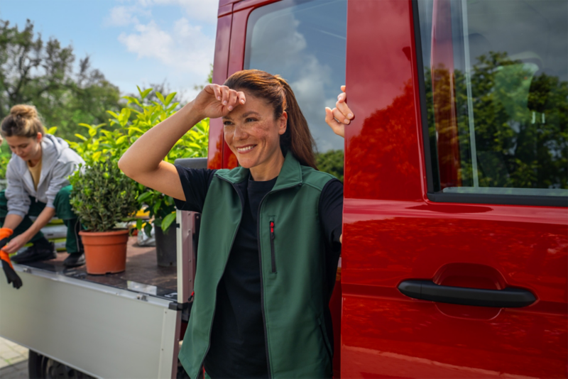 Ein roter VW Crafter Pritschenwagen, welcher mit Pflanzen beladen ist und Gärtnerinnen, die eine Pause machen.