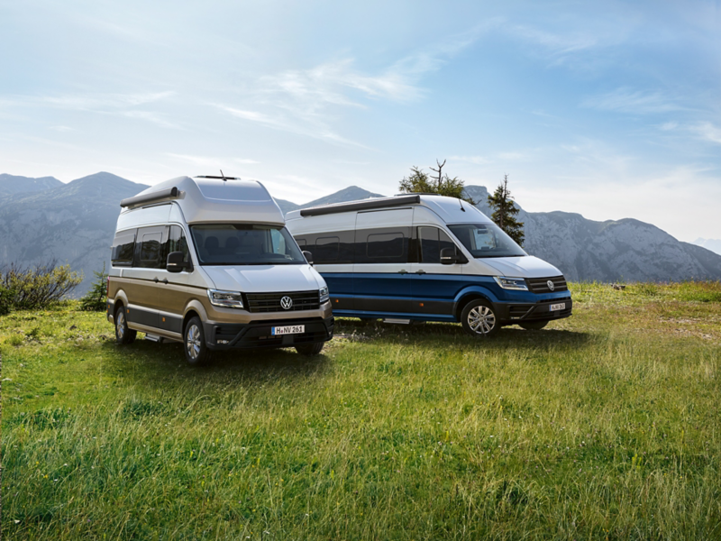 Der VW Grand California 600 und 680 parken auf einer Wiese mit einer Berglandschaft im Hintergrund