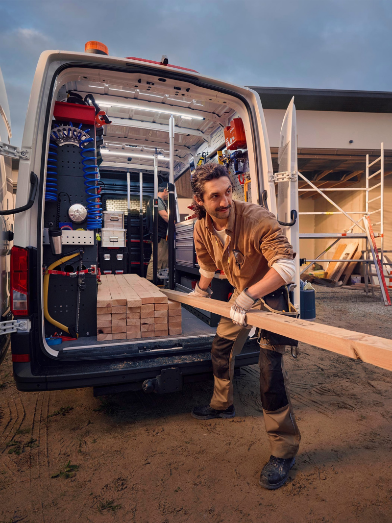 Ein Handwerker entlädt Holzlatten aus einem VW Crafter mit Regalausbau.