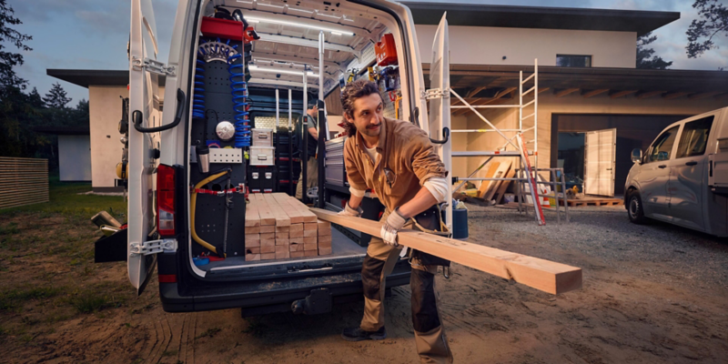Ein Handwerker entlädt Holzlatten aus einem VW Crafter mit Regalausbau.