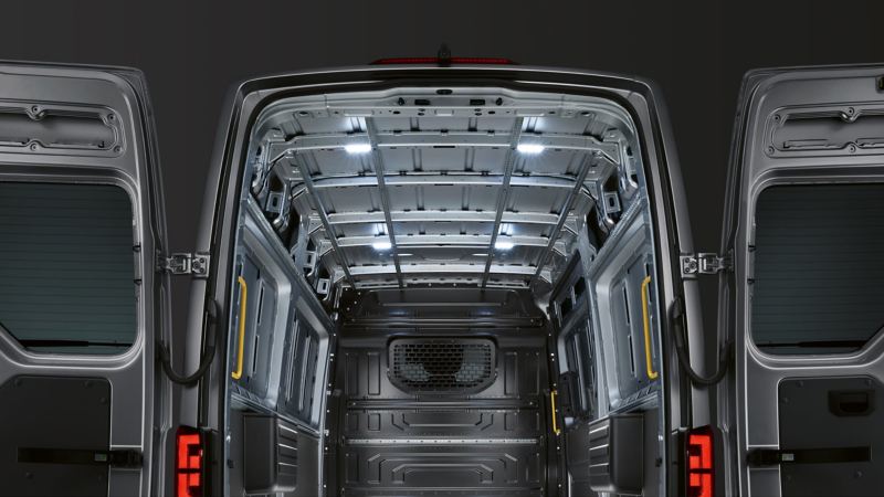 Crafter Furgone di Volkswagen è parcheggiato in un locale scuro. Le sue porte posteriori a battente spalancate consentono di dare uno sguardo al vano di carico. Quest’ultimo viene illuminato da quattro luci a LED installate sotto il tetto.