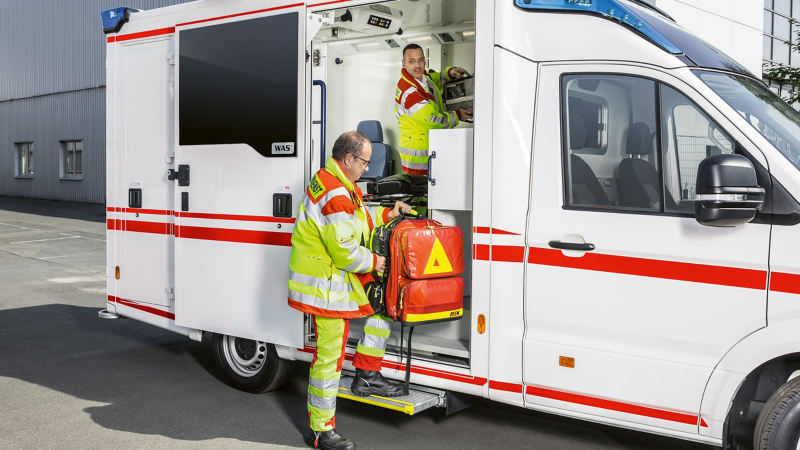 Ein VW Crafter als Blaulichtfahrzeug auf einem Parkplatz, ein Sanitäter lädt eine Tasche ein