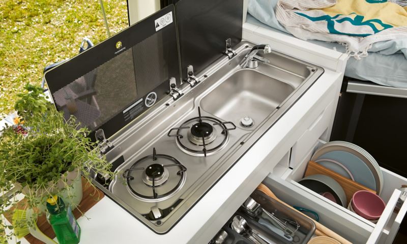 A gas powered hob with a drawer open underneath displaying utensils