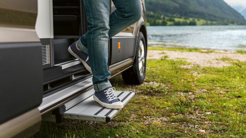 Gros plan sur le marchepied escamotable électrique devant un lac de montagne. Quelqu’un descend en toute décontraction.