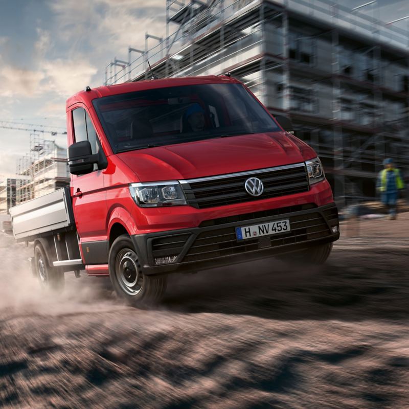 vw Volkswagen rød Crafter pickup med enkeltkabin og pickupplan kjører i fart over byggeplass med bygningsarbeidere i bakgrunn