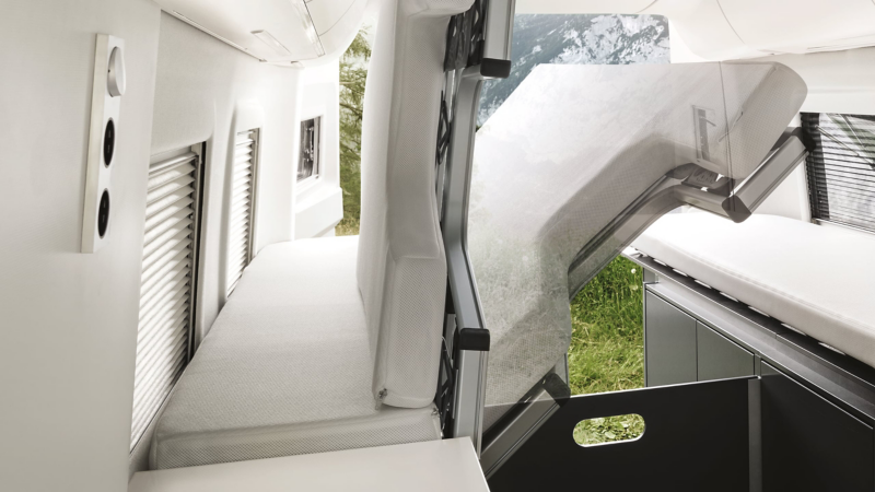 View into the rear of the Grand California 680. The lengthwise bed is folded up. Underneath we see the spacious storage space.