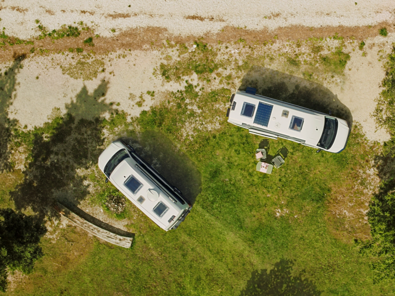Vogelperspektive auf zwei VW Grand California, welche an einem Strand parken.
