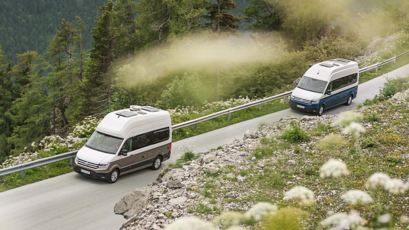 Ein VW Grad California 600 fährt hinter einem VW Grand California 680 eine Bergstraße entlang.