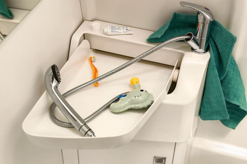 A close up of a sink with a showerhead and orange toothbrush resting on it 