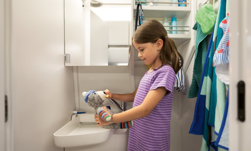 A young girl standing in the bathroom of the Grand California. She is brushing her teddy bear’s teeth.