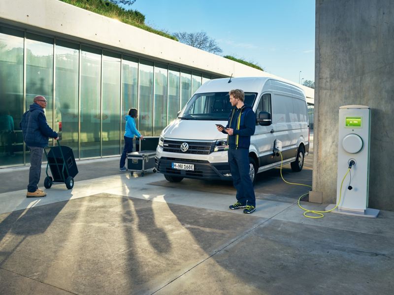 Bildet viser en hvit stor Volkswagen Crafter varebil som står parkert og tre håndverkere som laster og losser av varebilen