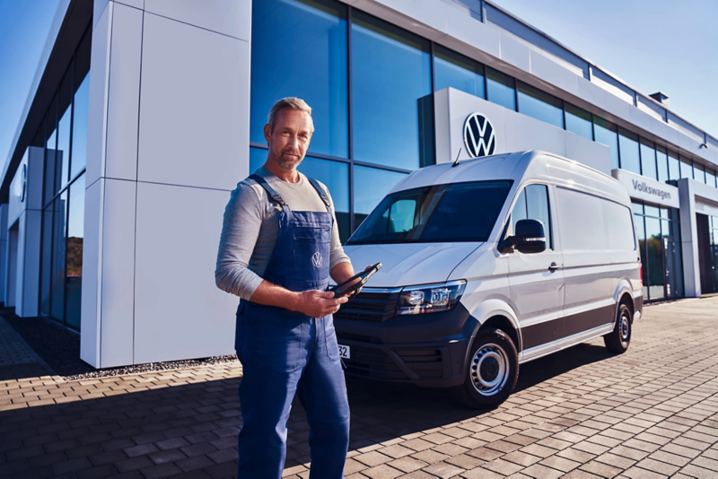 Pracownik serwisu na tle białego Volkswagena Craftera przed salonem.