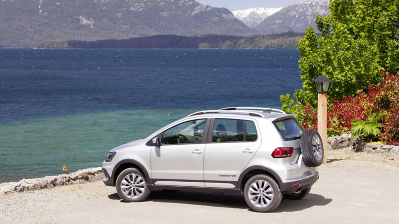 Une Volkswagen Crossfox avec sa roue de secours visible sur le coffre est garée de profil devant une étendu d'eau.