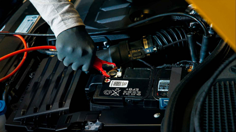 Experto de Volkswagen coloca pinza roja en la batería de carro.