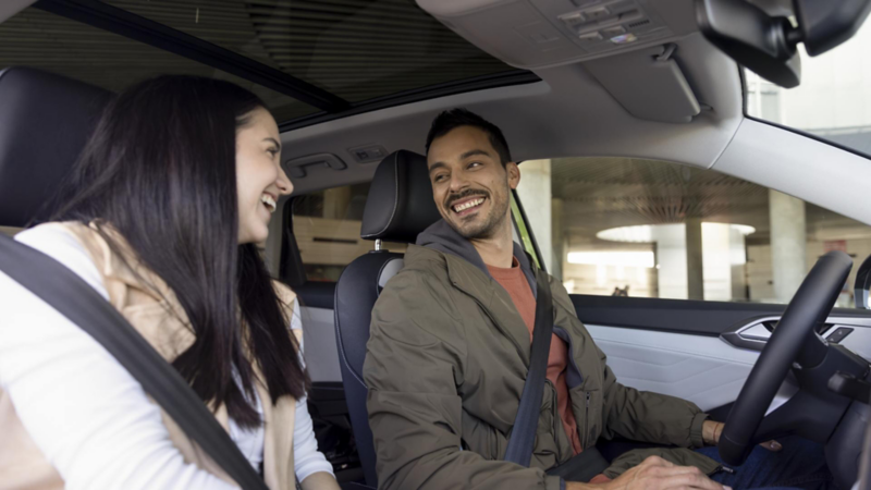 Pareja dentro de un auto Volkswagen sonríe.