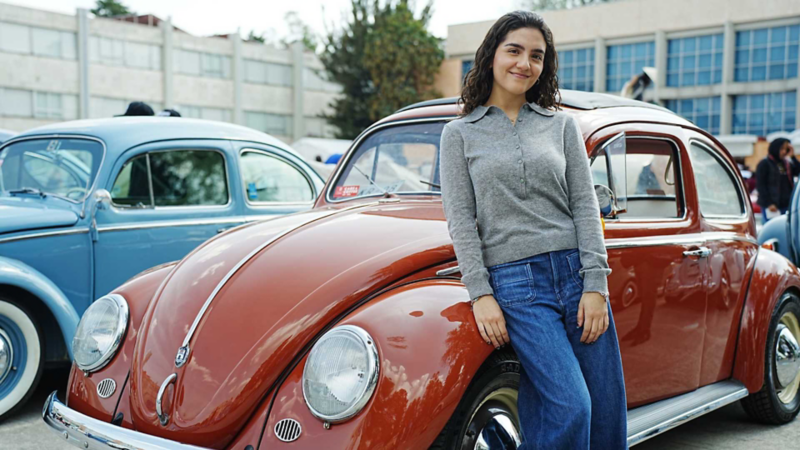 Joven se recarga en cofre de Volkswagen sedan clásico color rojo en exhibición.