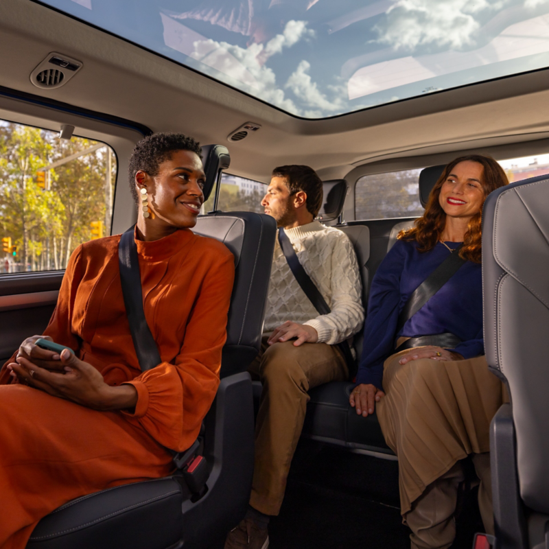 Tre personer sitter i en VW Caravelle under det stora panoramaglastaket.