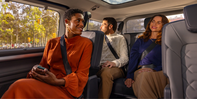 Three people sit in a VW Caravelle looking out through the panoramic glass roof.