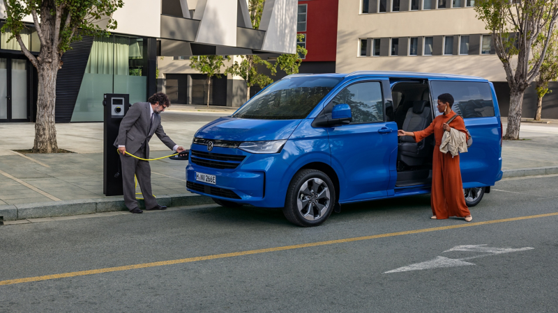 One person plugs the charging cable into the VW Caravelle and one person closes the sliding door of the VW Caravelle.