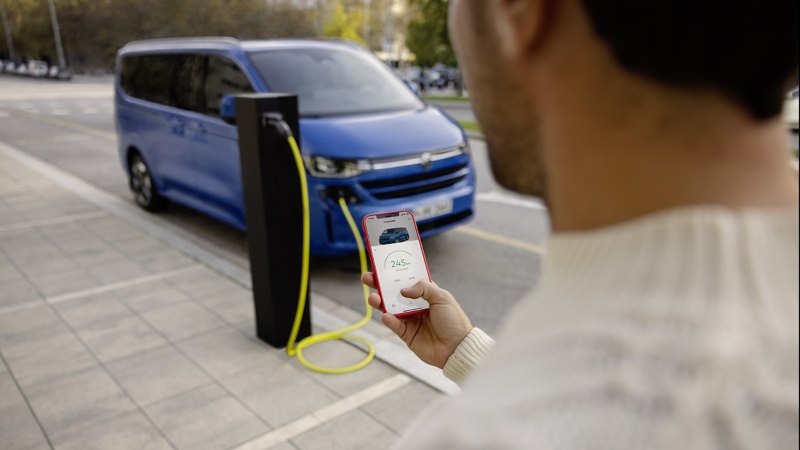 A man looking at a smartphone while standing near a charging Transporter Shuttle