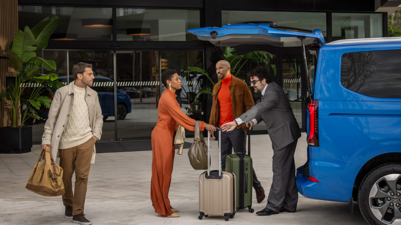 Four people moving luggage into the rear of the VW Shuttle.