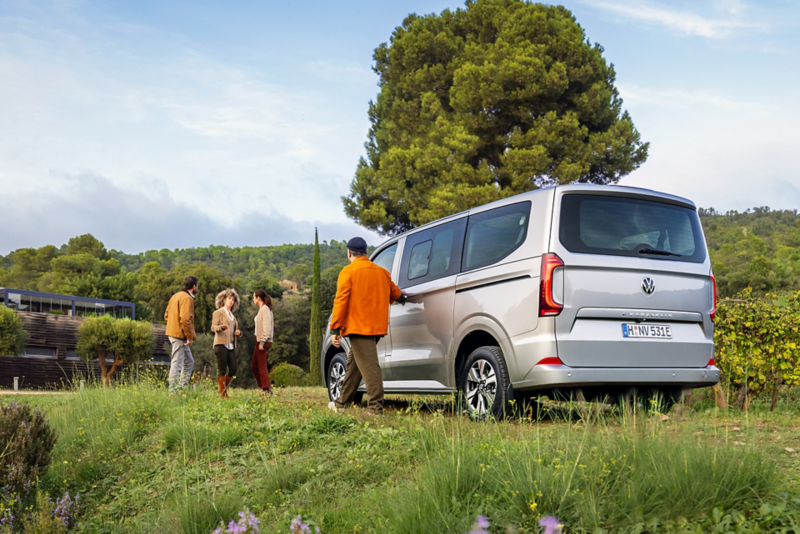 Ein VW Caravelle parkt auf einer Wiese wo sich Freunde treffen.