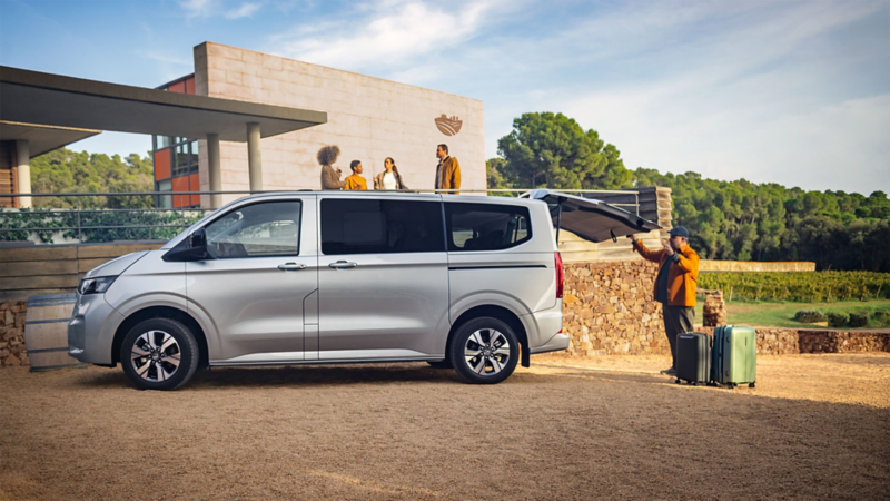 La VW Caravelle est garée devant un batiment avec le coffre ouvert et des personnes se tiennent près d'elle.